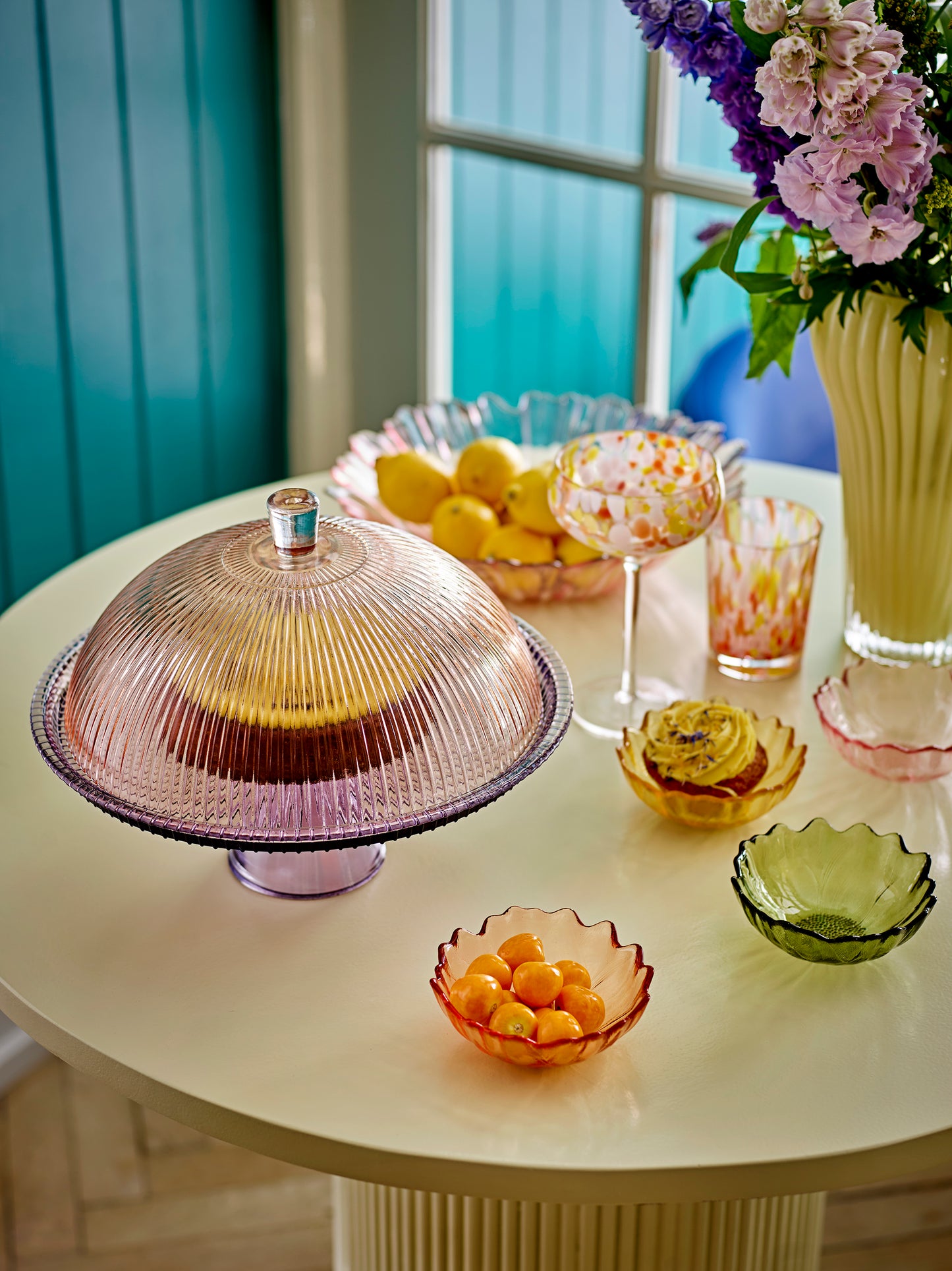 Decorative table setting with a glass cloche, bowls of fruit, and a vase of flowers.