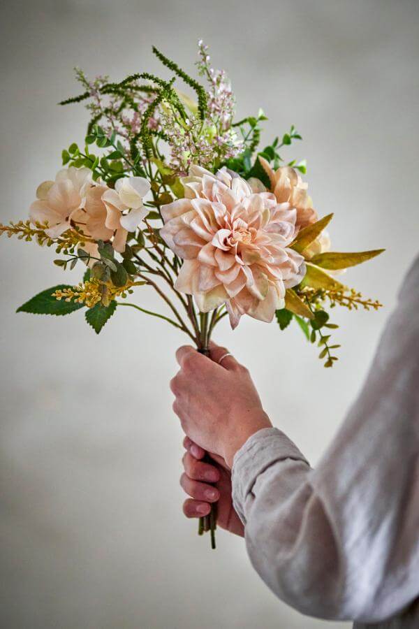 Hand holding a bouquet of flowers against a plain background