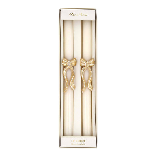 A boxed set of two ivory taper candles with gold bow details, presented in a tall white gift box with the brand name 'Mia Mari' visible at the top.