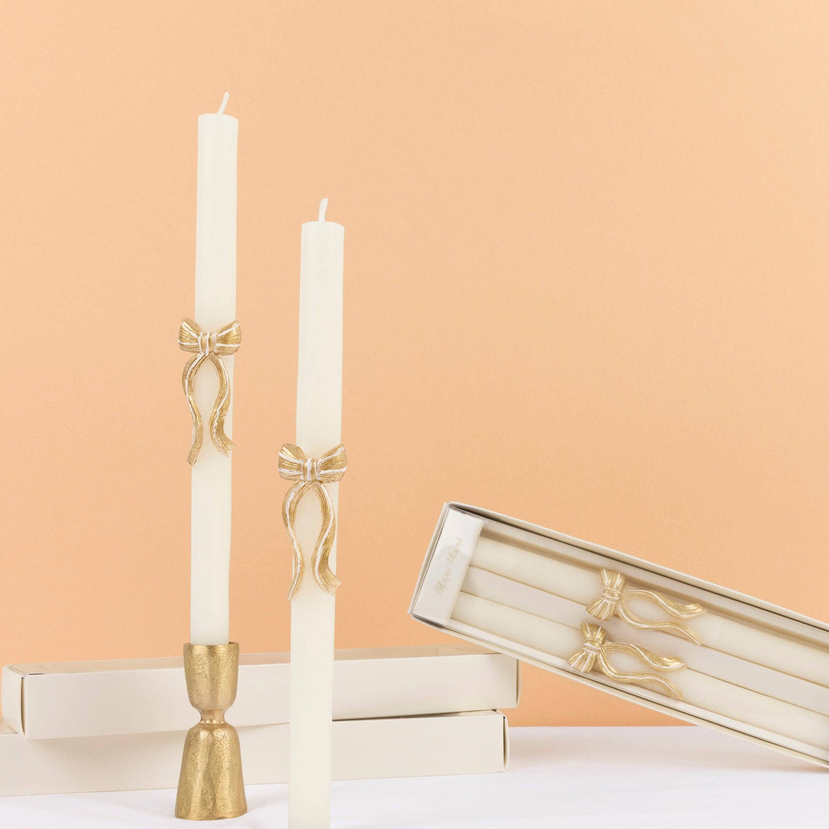Two taper candles with gold bow details in candle holders on a table