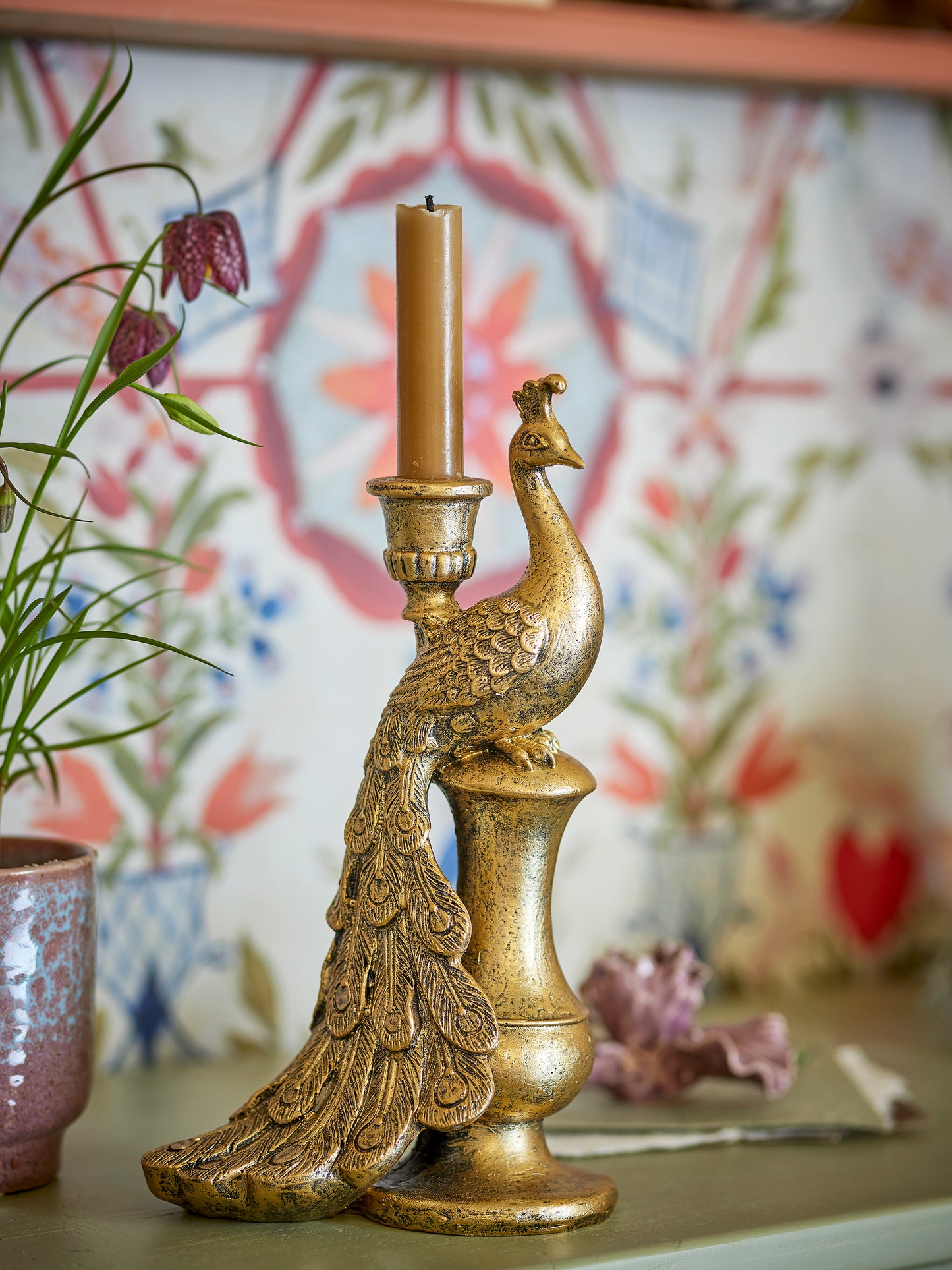 Gold peacock-shaped candle holder with an unlit candle on a decorative surface.