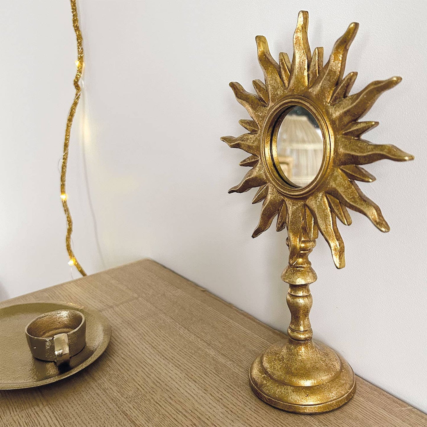 Decorative gold sun-shaped mirror on a wooden surface with a white wall background