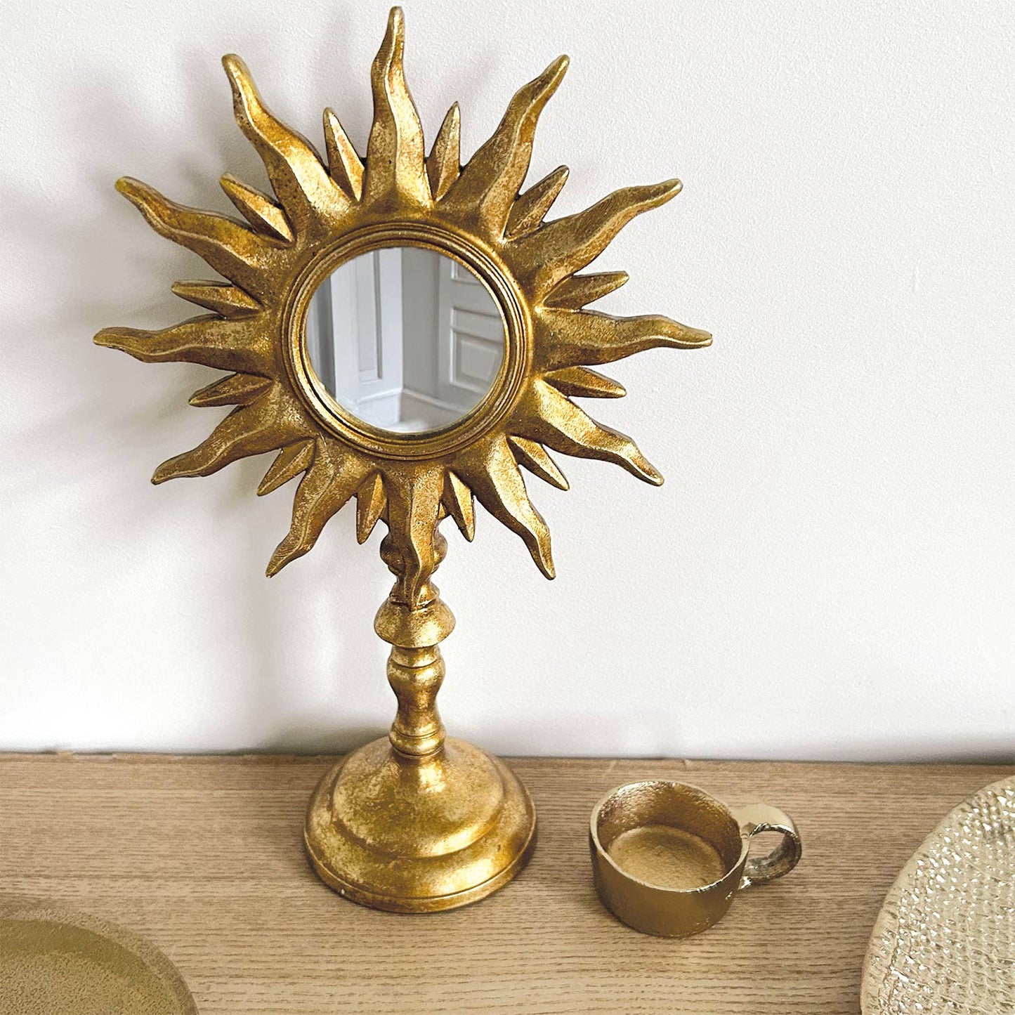 Decorative gold sun-shaped mirror on a wooden surface with a white wall background