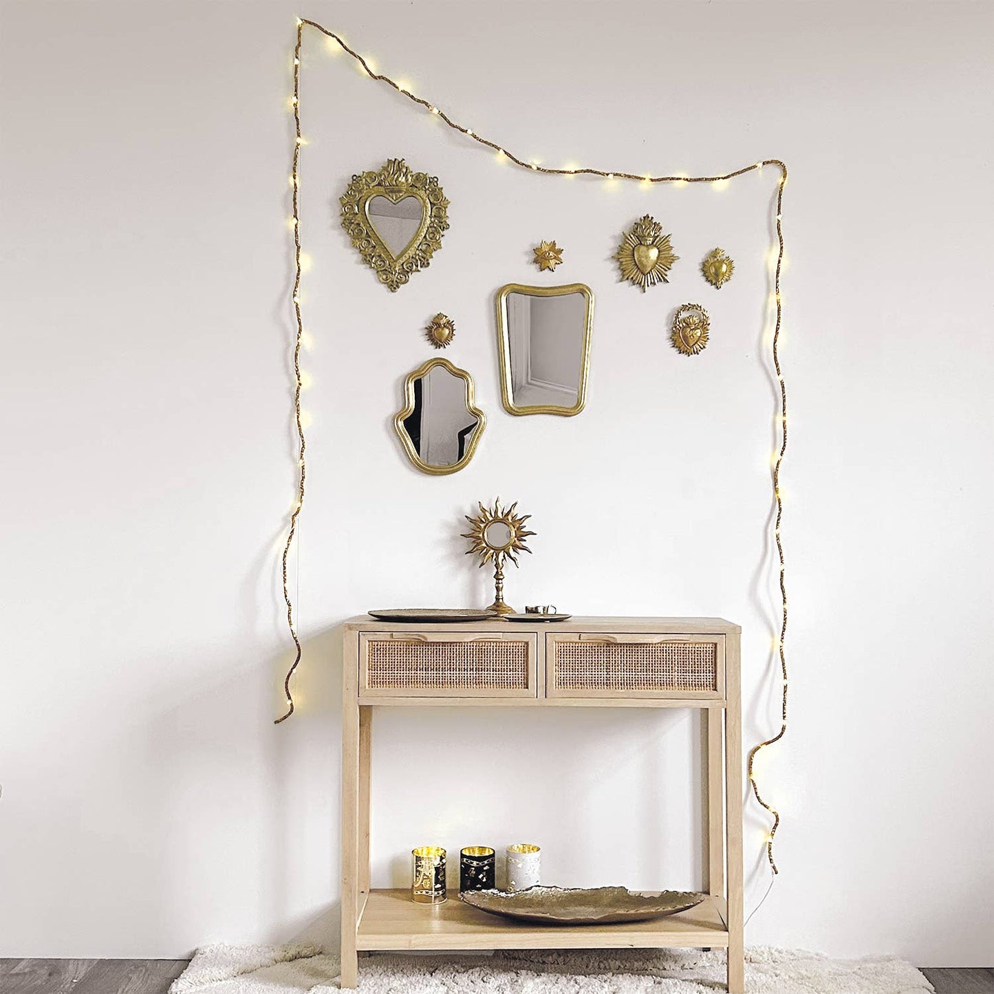Decorative console table with mirrors and string lights against a white wall.