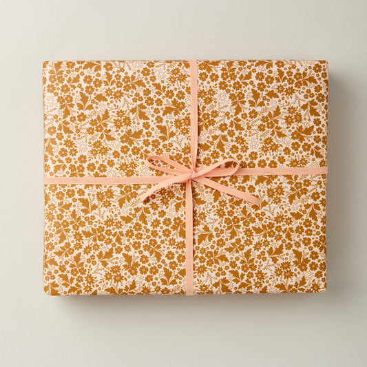 A sheet of golden gift wrapping paper with a floral print, tied with a pink ribbon.
