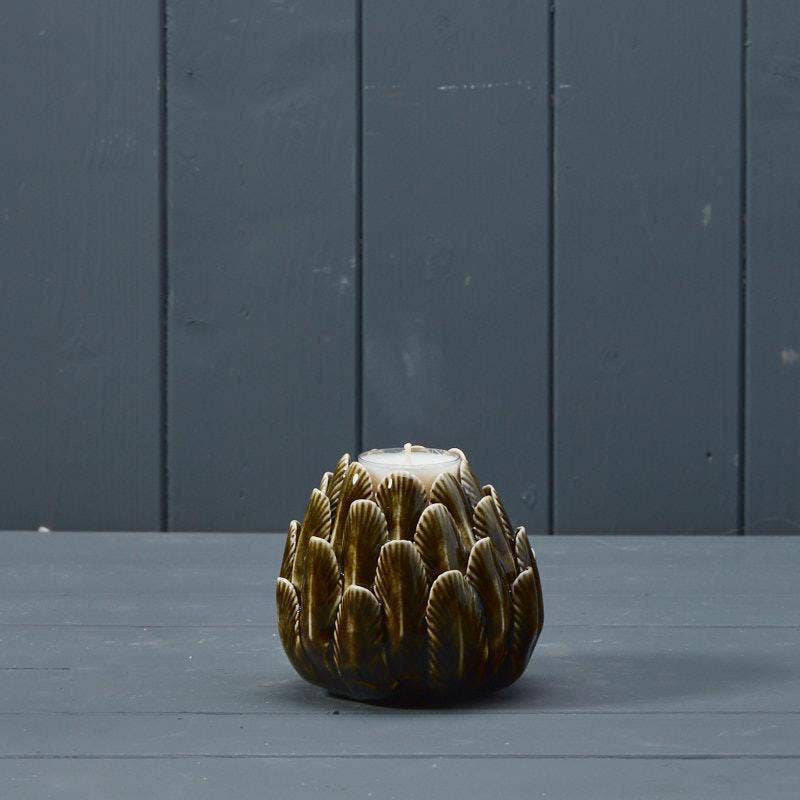 A small sculptural candle holder shaped like a textured artichoke, featuring a glossy dark brown and gold glaze with a white wax top, set against a dark gray paneled background.