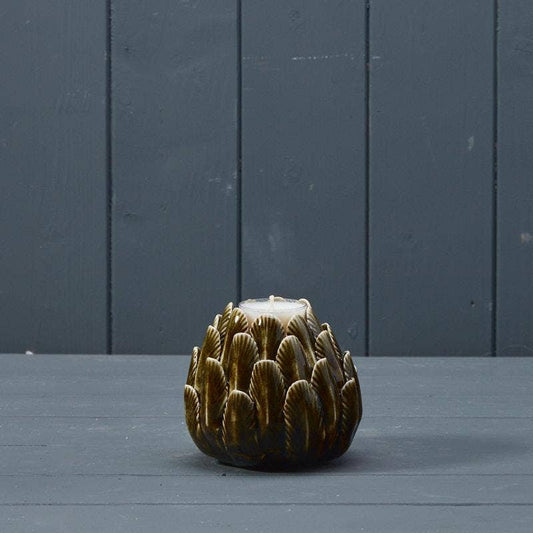 A small sculptural candle holder shaped like a textured artichoke, featuring a glossy dark brown and gold glaze with a white wax top, set against a dark gray paneled background.