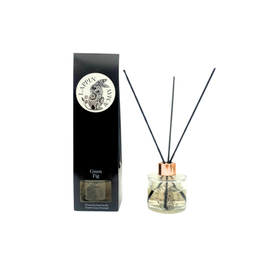 A black reed diffuser with a clear glass container and a copper-colored top, alongside its black packaging box with a decorative seal.