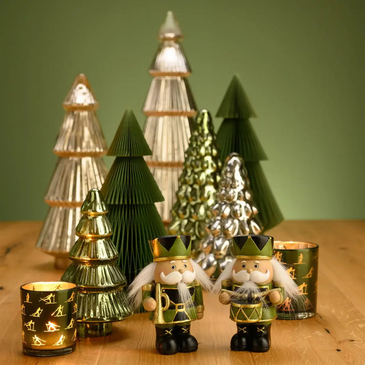 Decorative Christmas trees and figures on a wooden surface with a green background