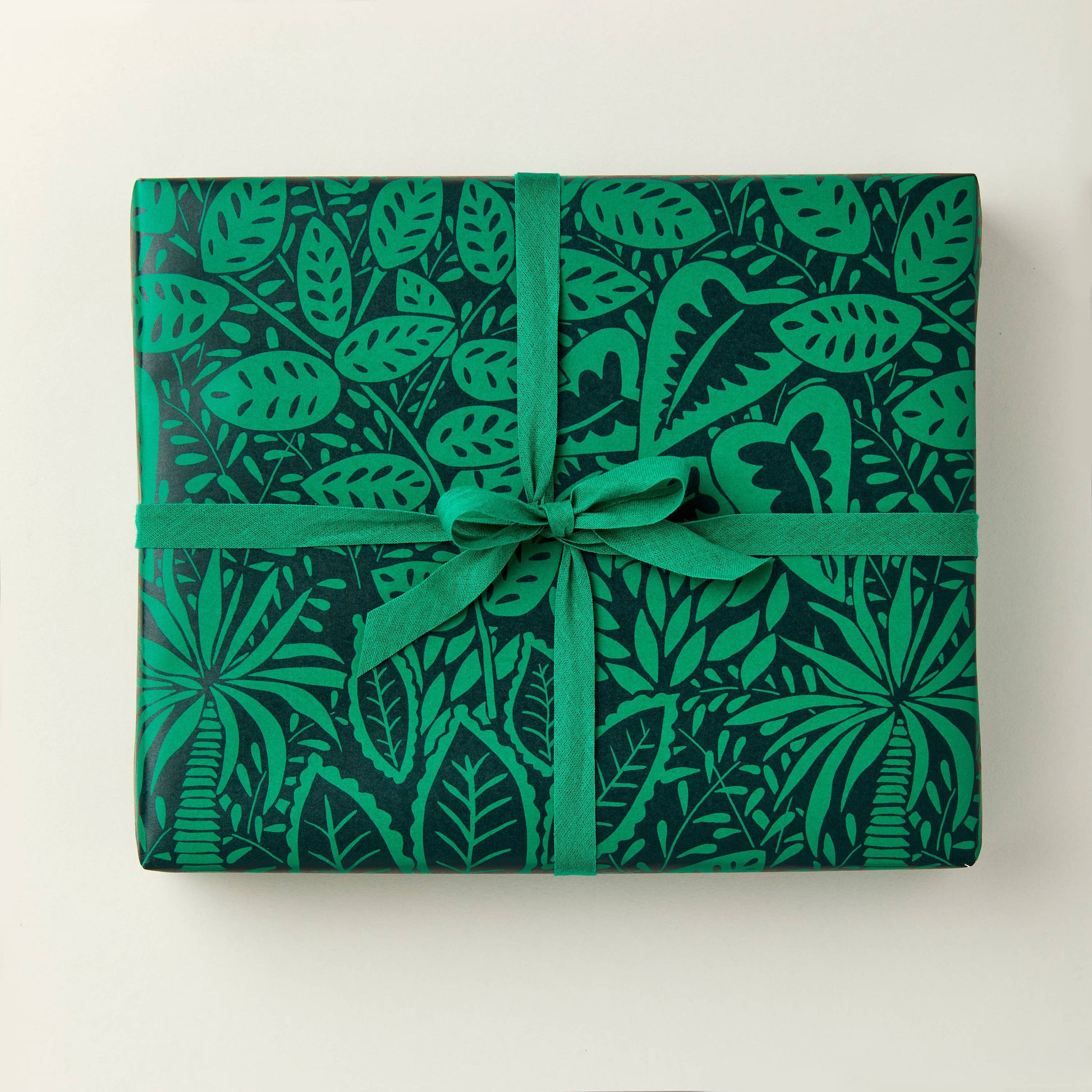 A sheet of green gift wrapping paper with a leaf pattern, tied with a green ribbon.