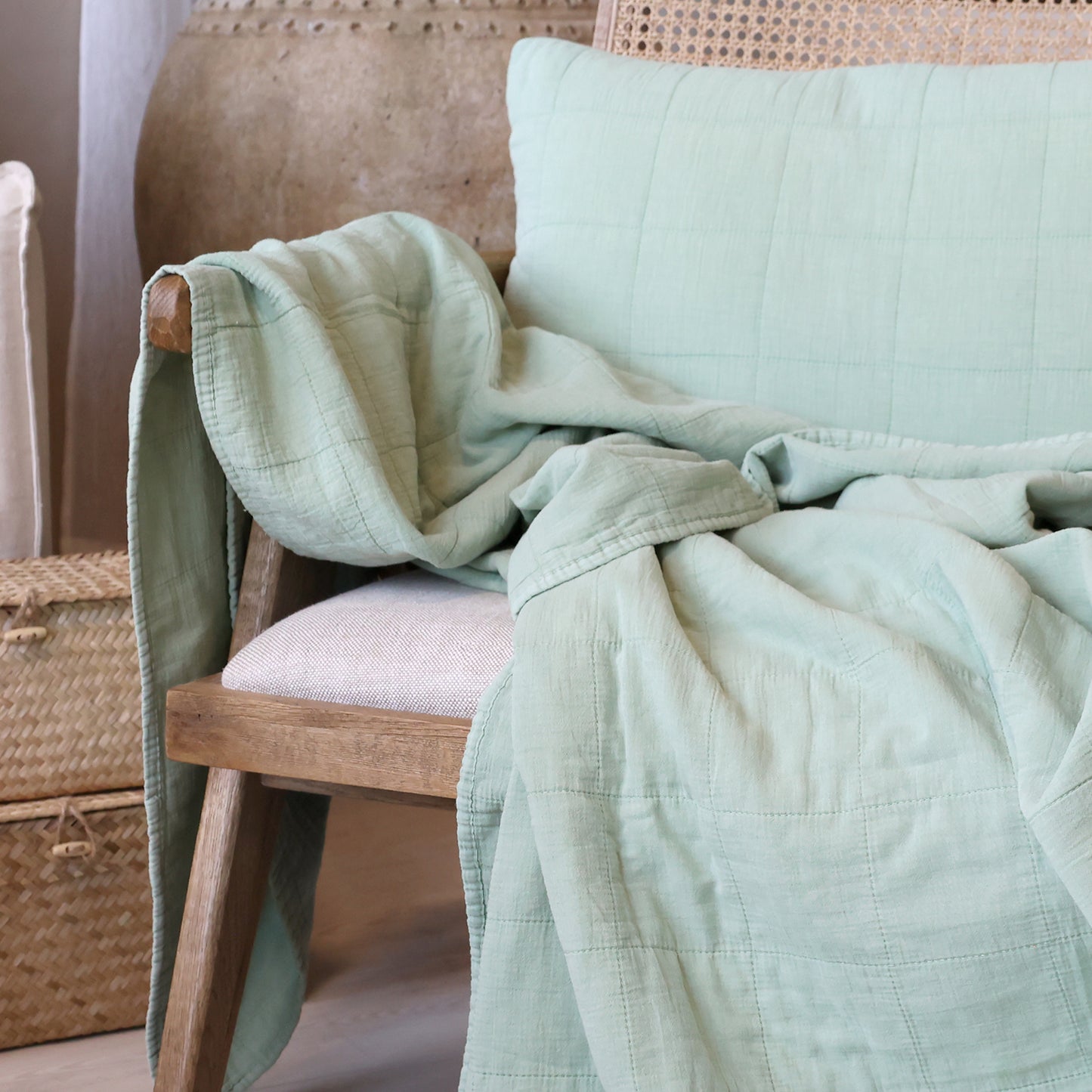 Light green quilt draped over a wooden chair with a neutral background