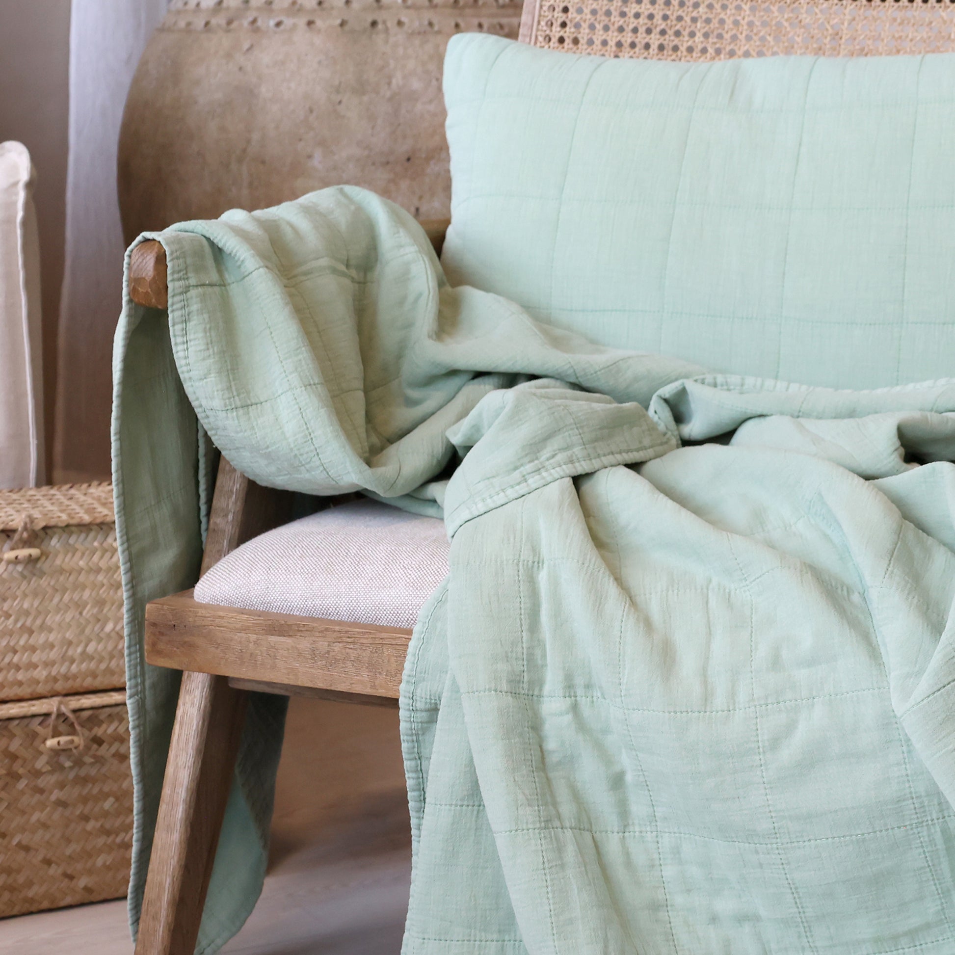 Light green quilt draped over a wooden chair with a neutral background