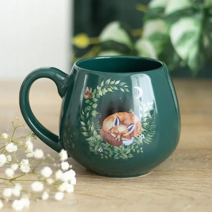 Green mug with fox design on a wooden surface with flowers and leaves in the background