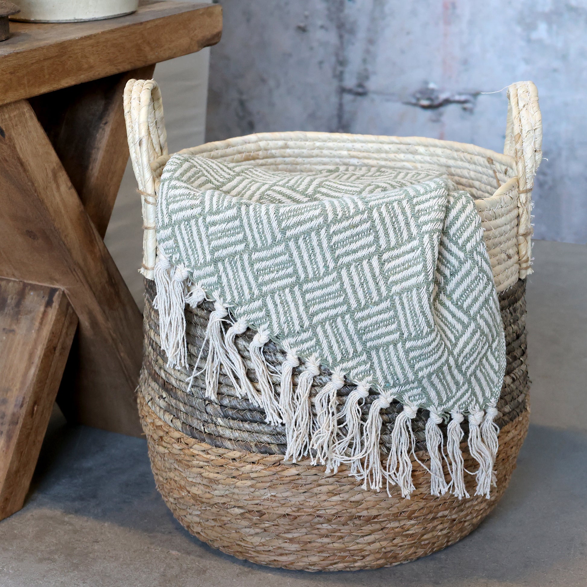 Woven basket with a textured blanket draped over it, placed on a wooden surface.