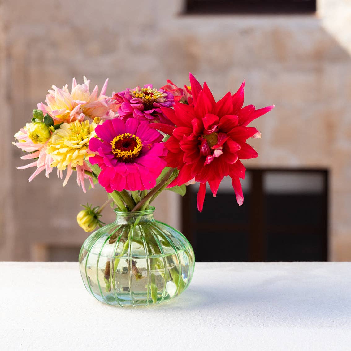 Green glass bud vase 8cm with flowers on table top