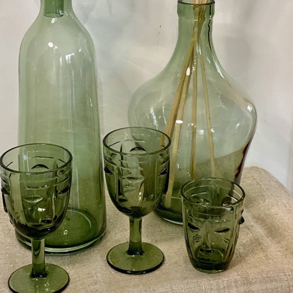 Green glassware including bottles and glasses on a textured surface with a neutral background