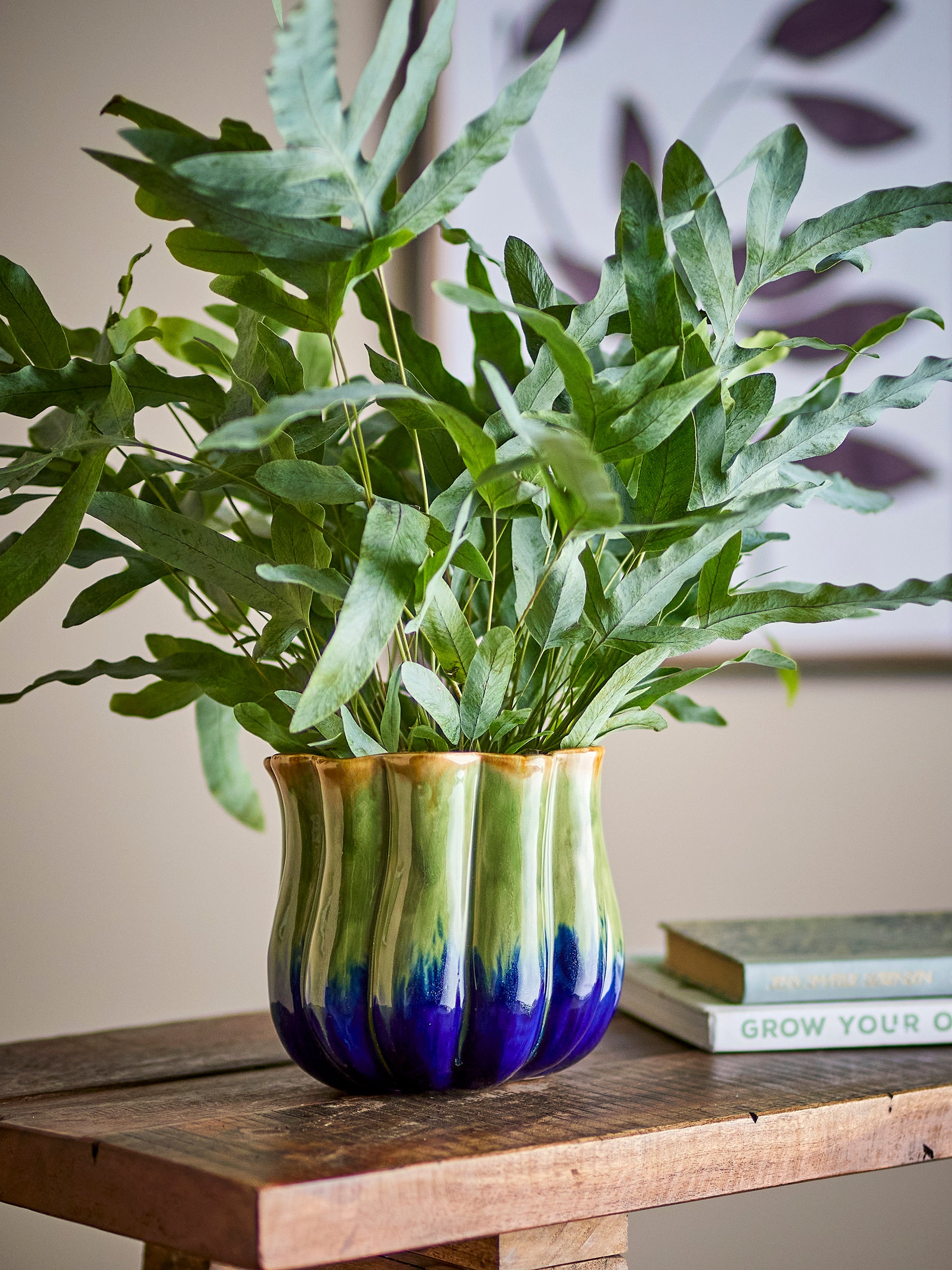 Green and blue ceramic vase with a plant on a wooden surface
