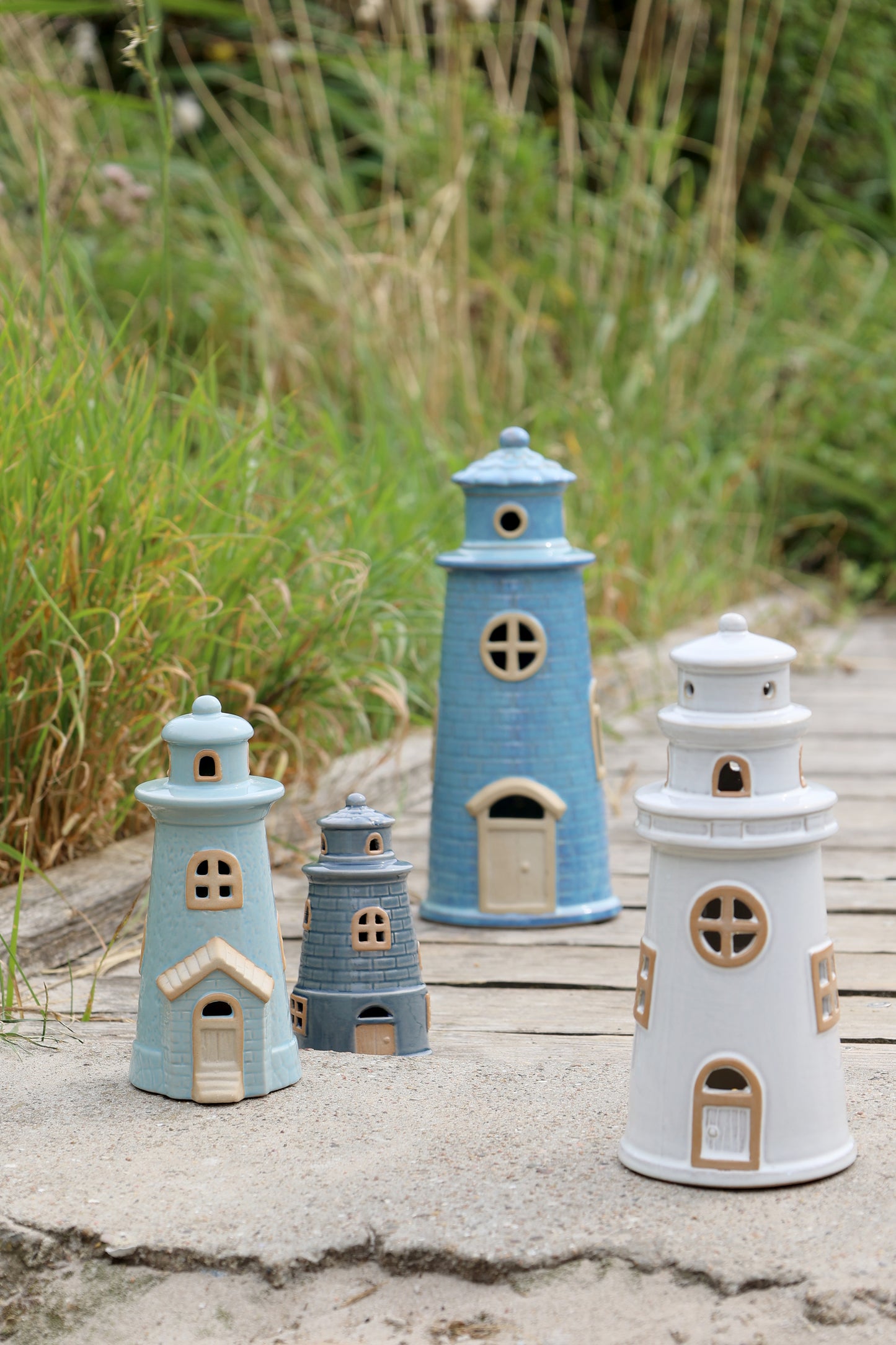 Set of ceramic lighthouse figurines in various sizes on a wooden surface with grass in the background.