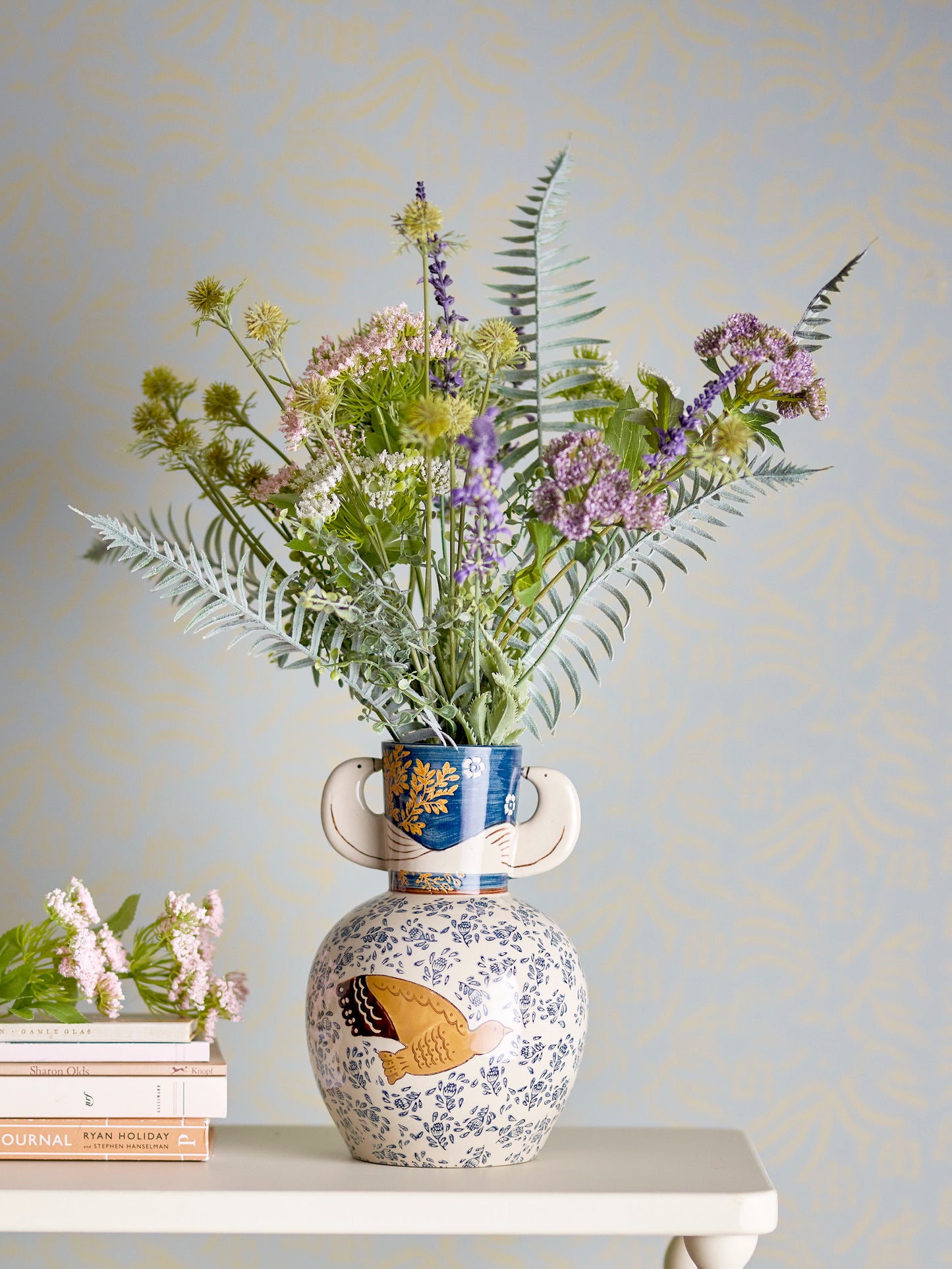 Decorative vase with floral arrangement on a table against a light blue wall.