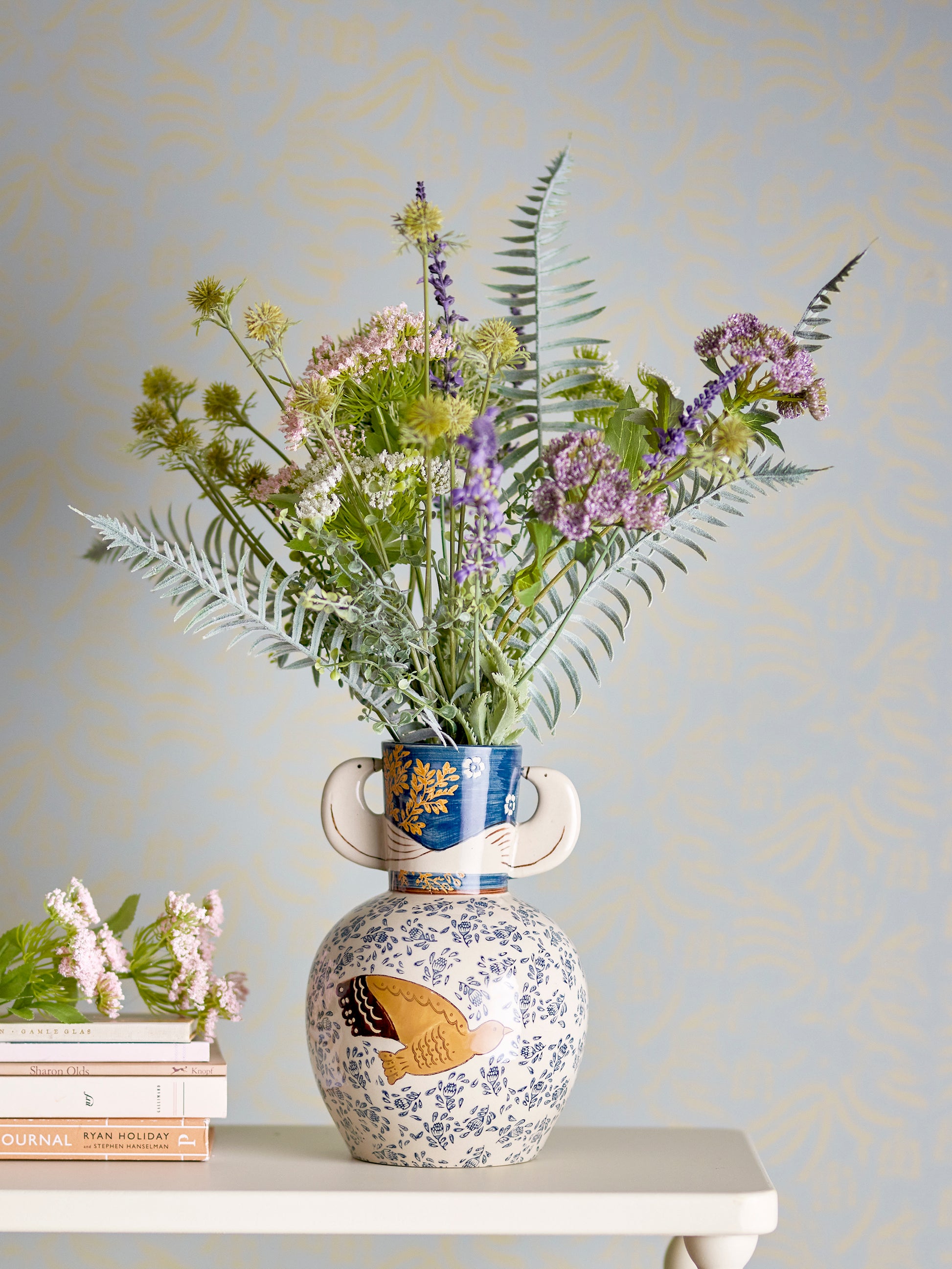 Decorative vase with floral arrangement on a table against a light blue wall.