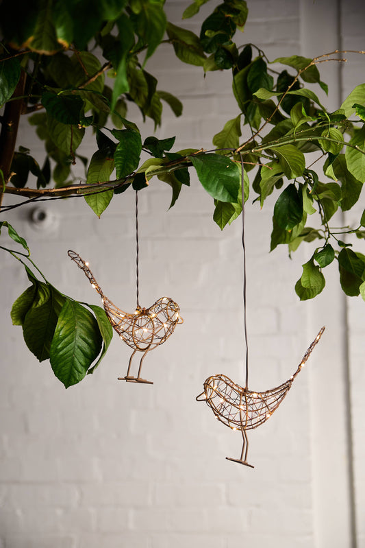 Decorative wire birds hanging from a branch with green leaves on a light background