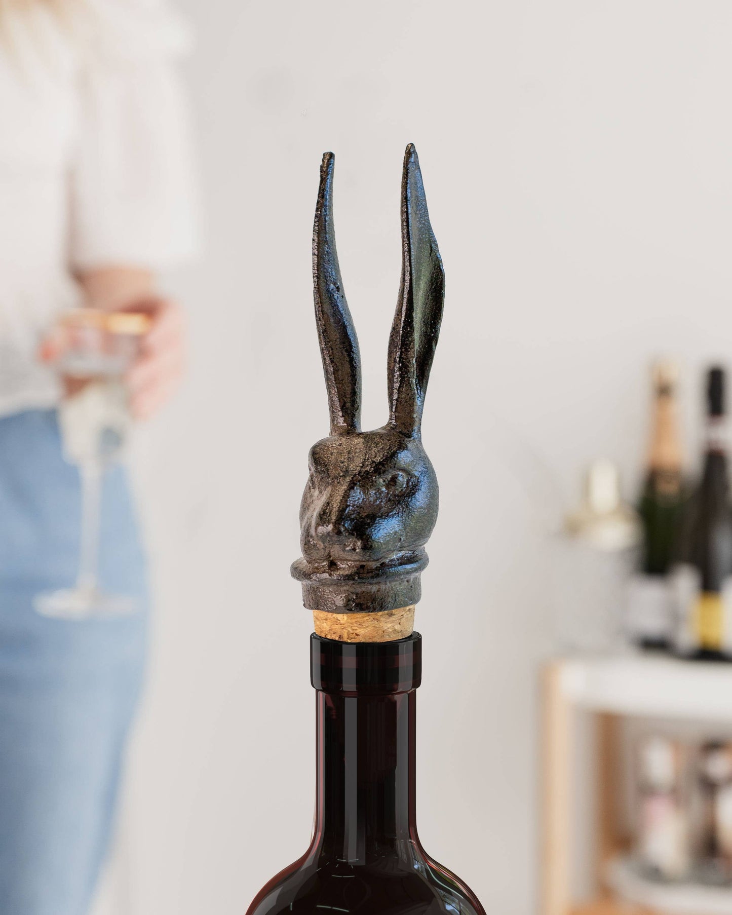 Decorative wine bottle stopper with animal head design on a bottle, blurred background of a person holding a glass.