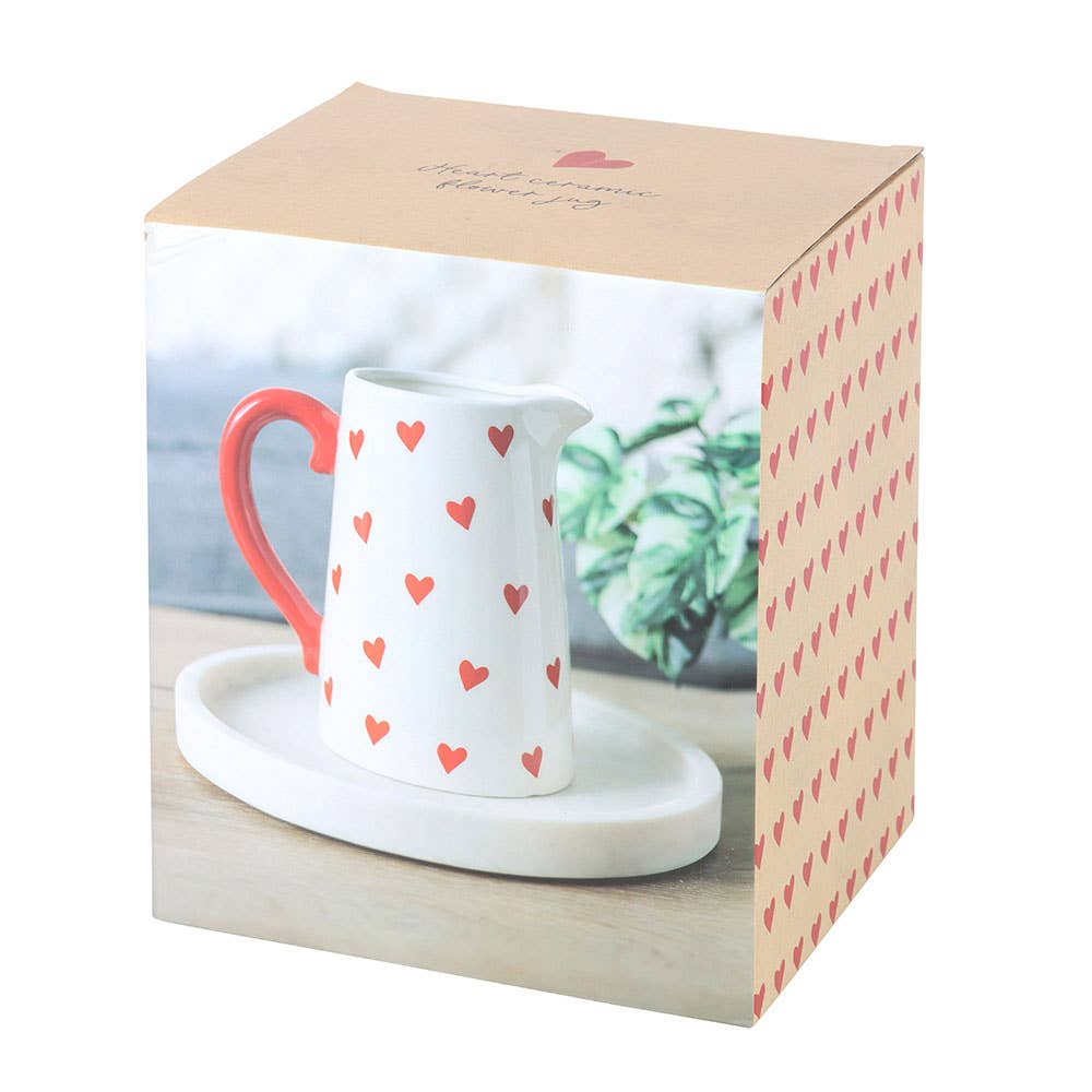 White ceramic pitcher with red heart patterns on a white plate, inside a decorative box.