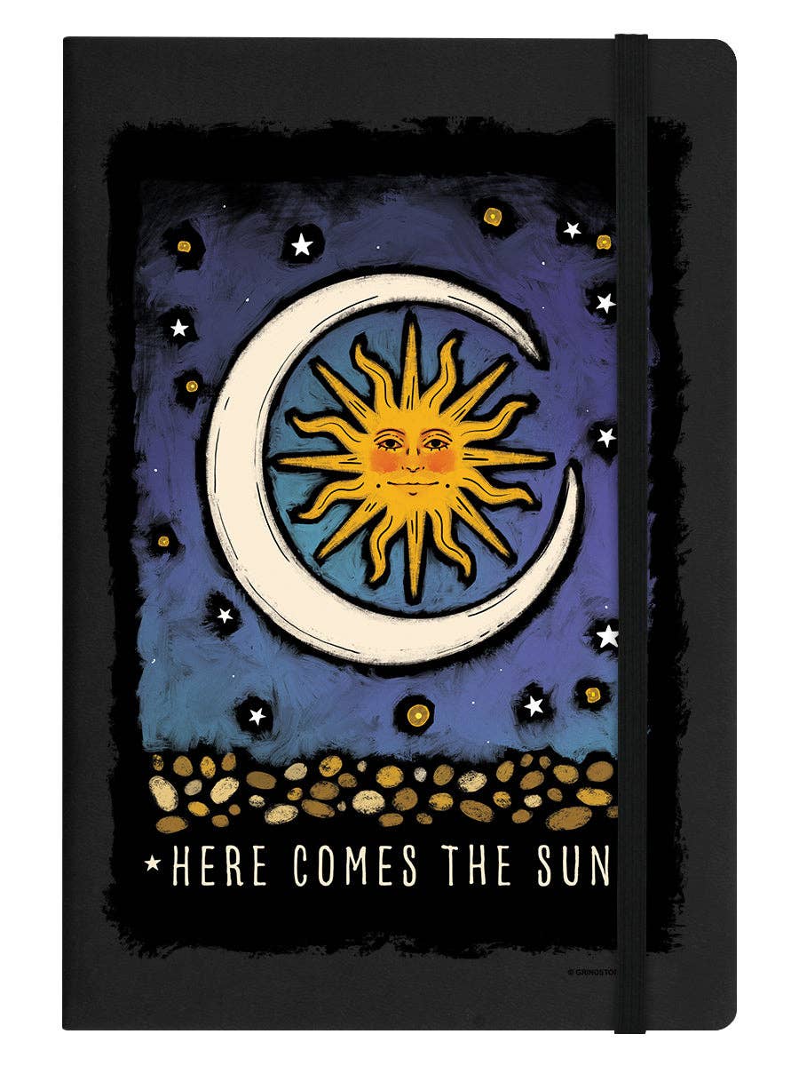 Black notebook with sun and moon design and 'Here Comes the Sun' text on a dark background