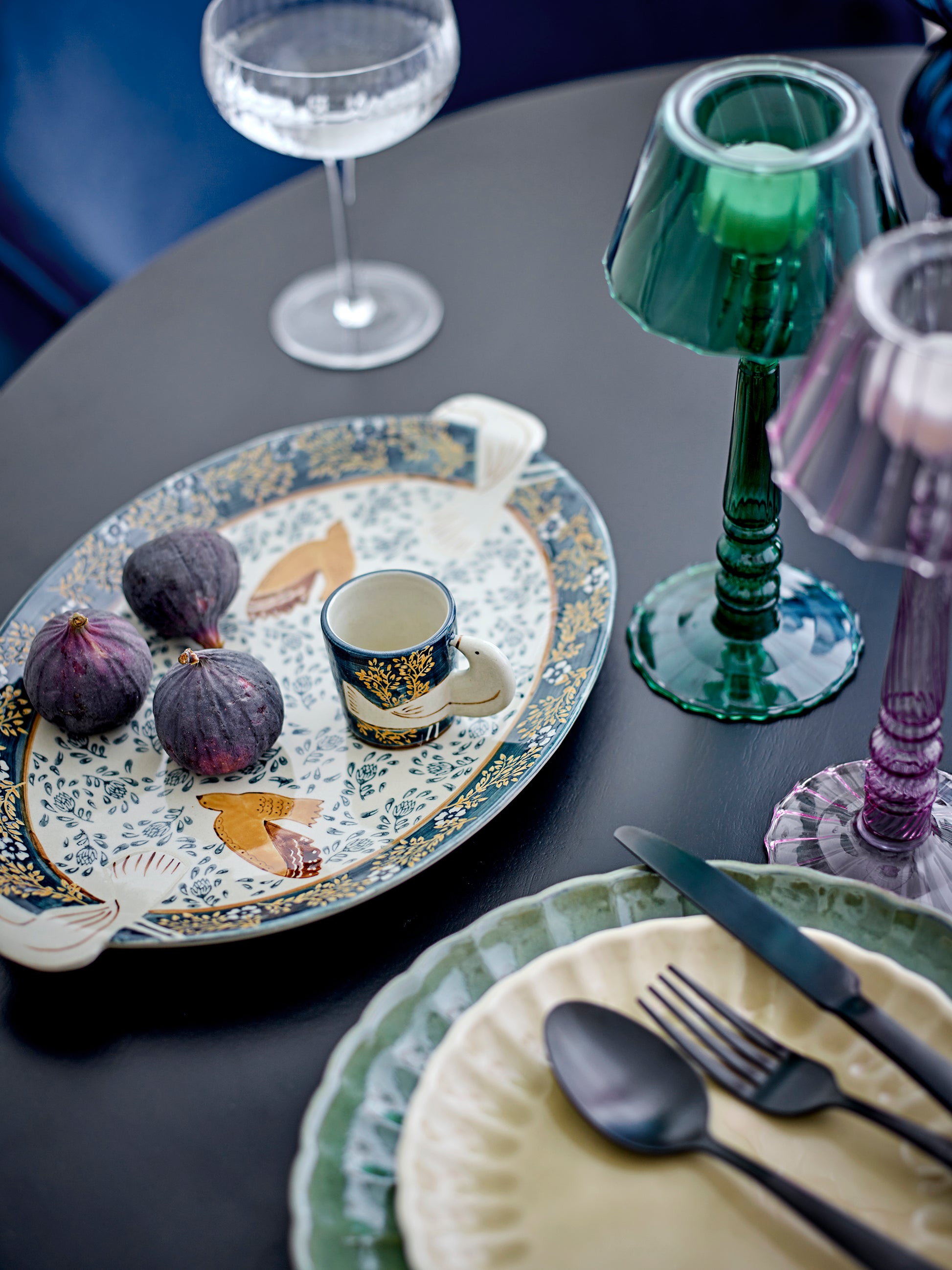 Dining table setting with a decorative platter, cups, and cutlery on a dark surface.