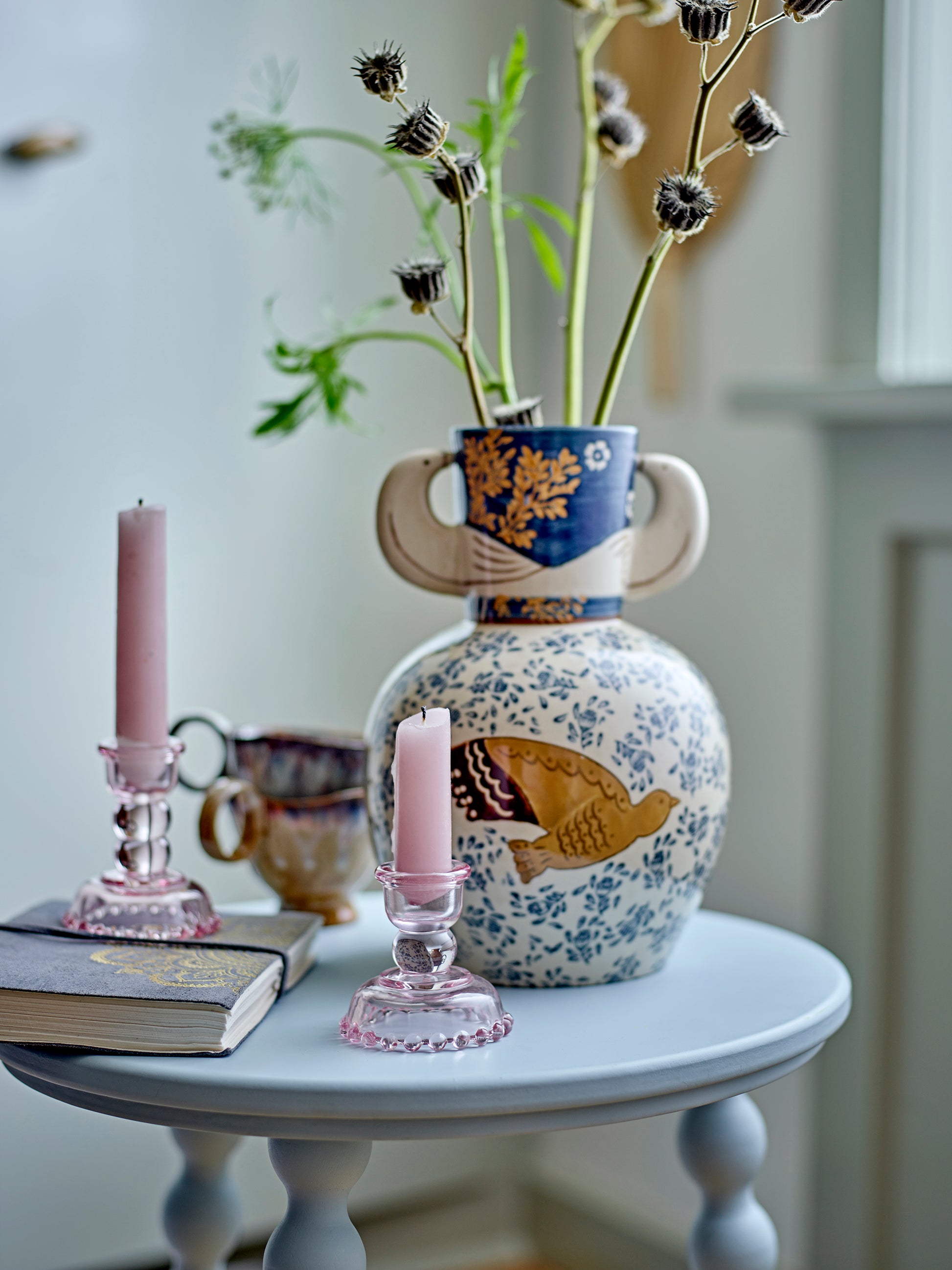 Decorative vase with floral patterns on a small round table with candles and books.