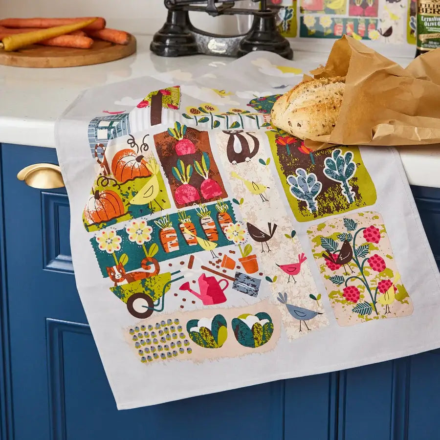 Colorful kitchen towel with nature-themed design hanging on a blue cabinet.