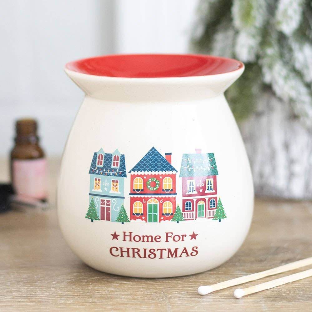 A ceramic Christmas oil burner with a red interior and exterior holiday illustration of colorful houses and the text 'Home For CHRISTMAS'.