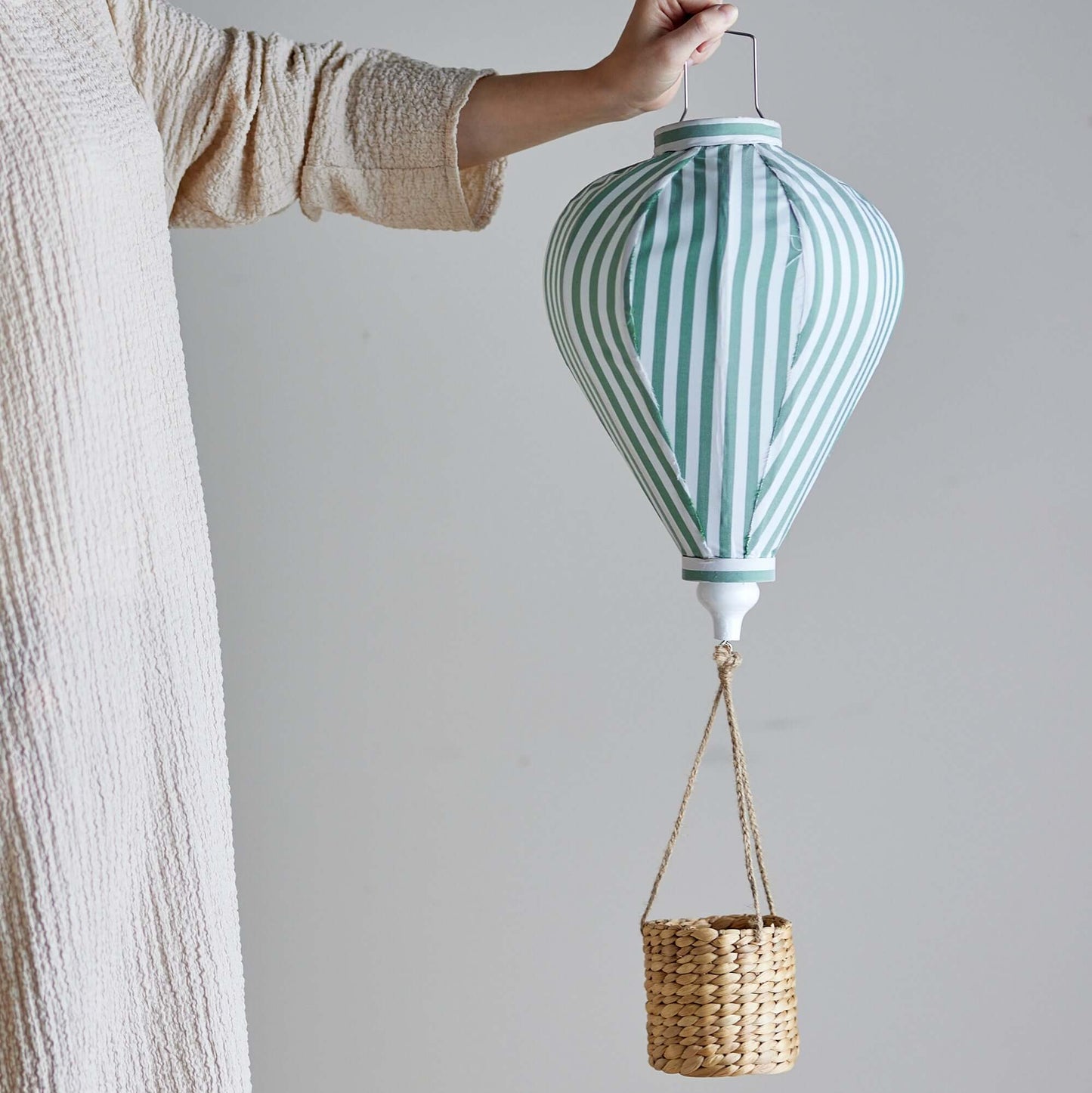 Person holding a striped lantern with a basket attached against a plain background