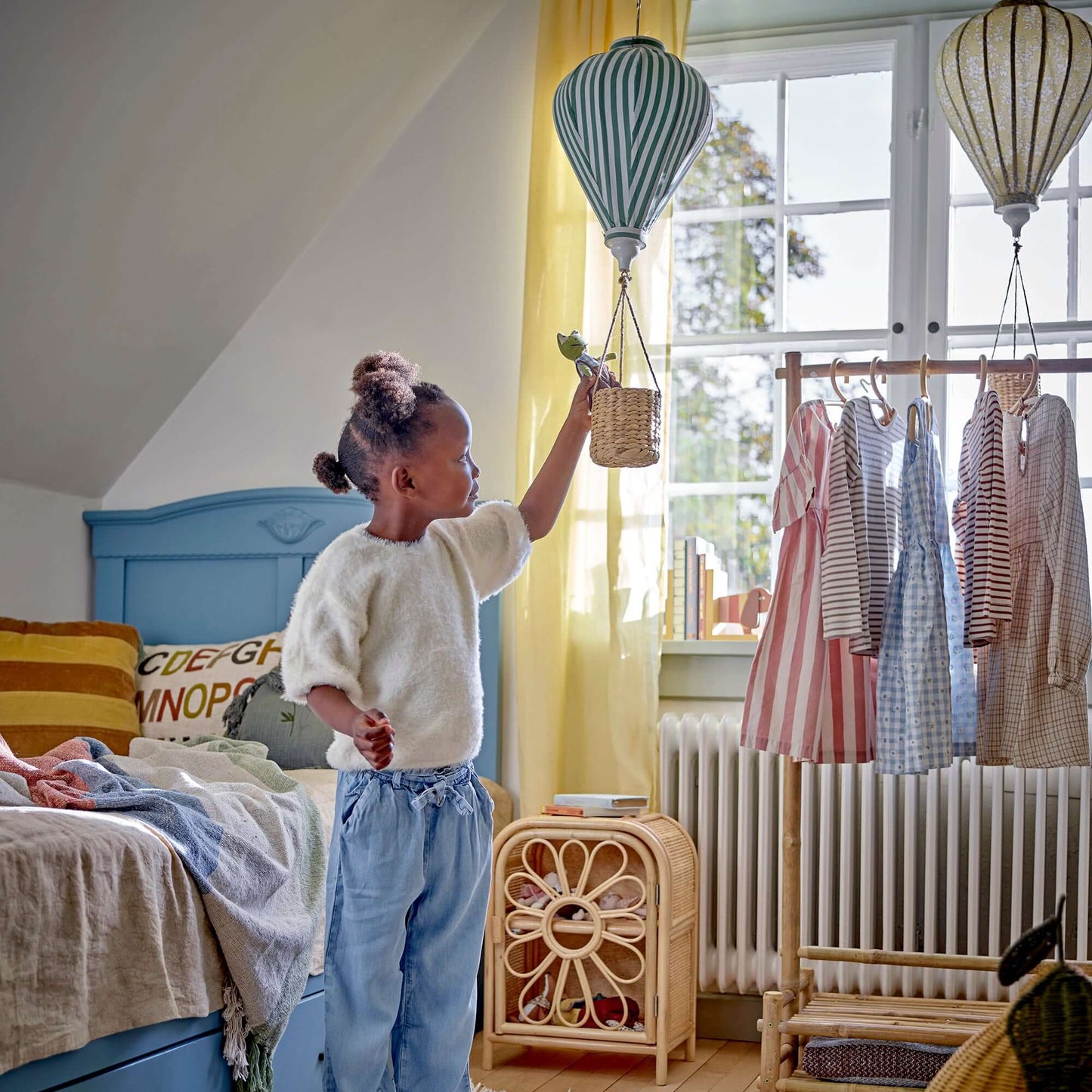 Child in a bedroom with colorful decor, including a polka dot rug and hot air balloon decorations.
