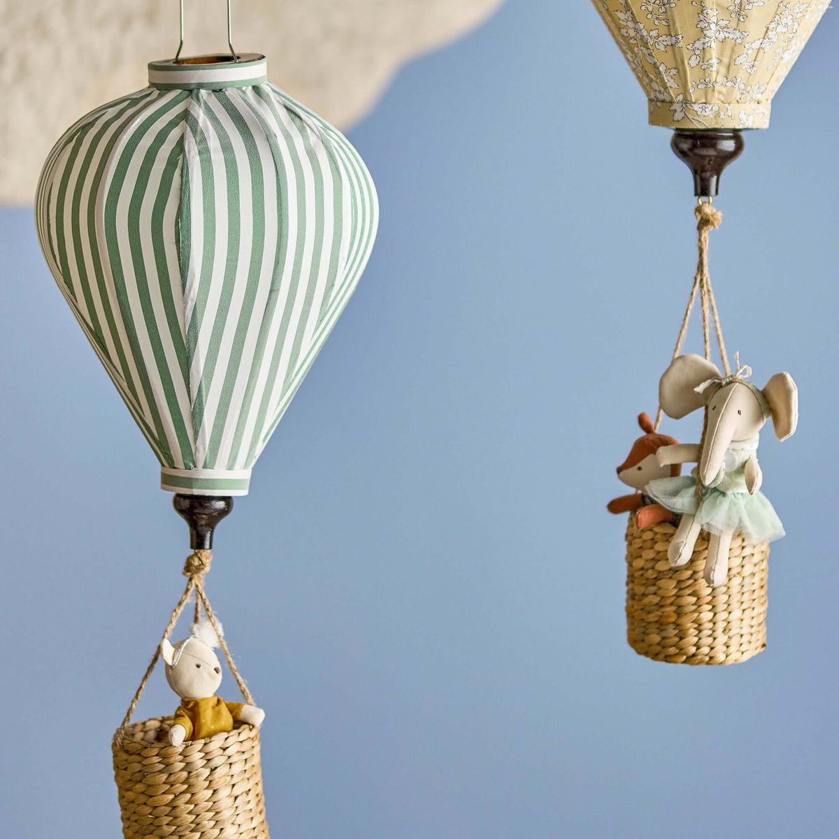 Two hot air balloons with toy figures in baskets against a blue sky.