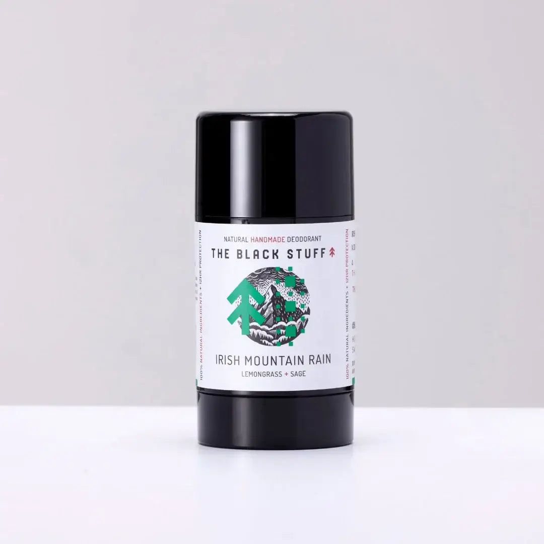 A stick deodorant labeled 'The Black Stuff - Irish Mountain Rain' in a black container with a white and green label showing the product name and a graphic of an Irish landscape.