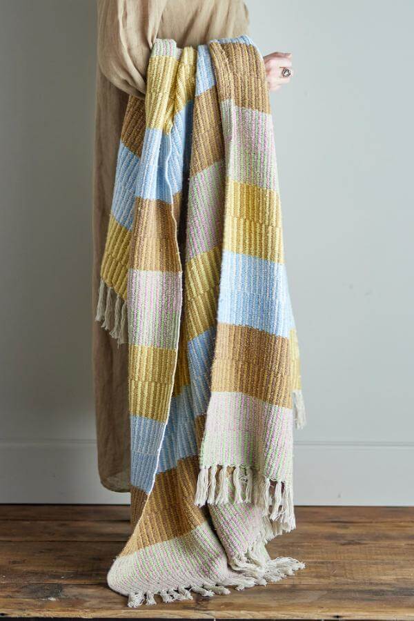 Colorful striped throw held by a person against a neutral background