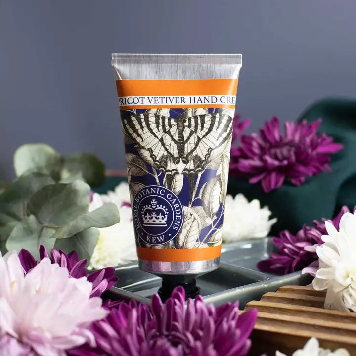 Hand cream tube with floral and garden-themed design on a table with flowers.