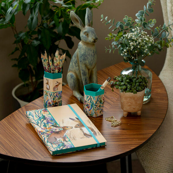 Decorative items on a round wooden table including a notebook, pencils, and a rabbit figurine.