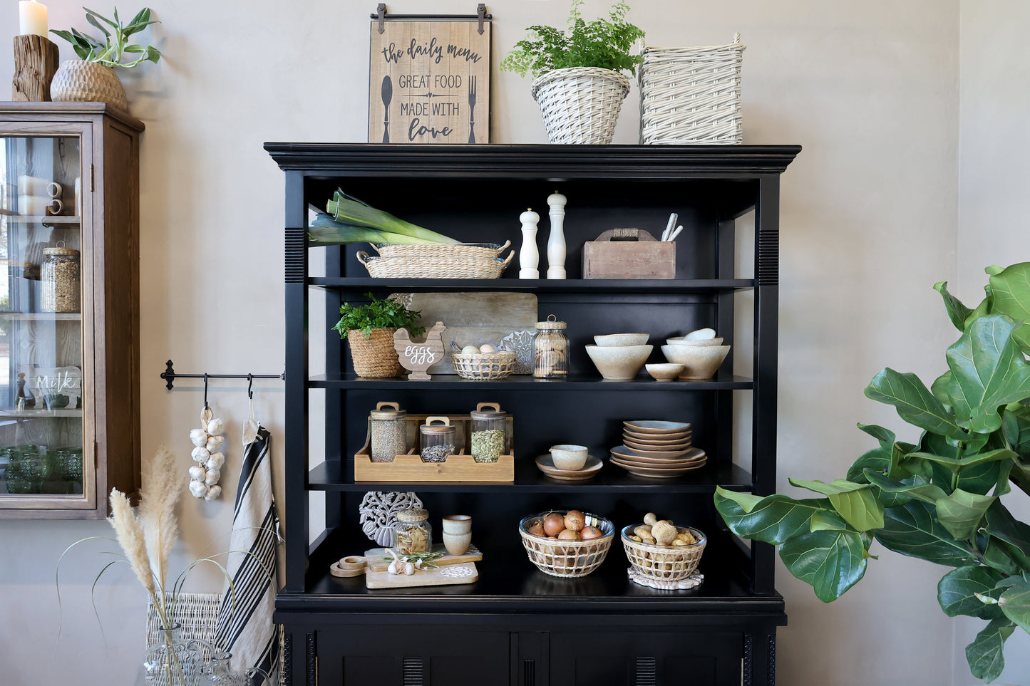 Black bookshelf with decorative items in a room with plants and a cabinet.