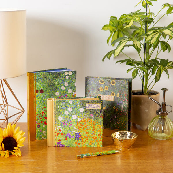 Decorative notebooks with floral designs on a wooden surface with a plant and lamp in the background.