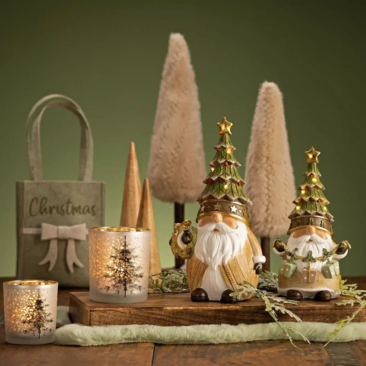 Decorative Christmas scene with gnomes, candles, and trees on a wooden surface.