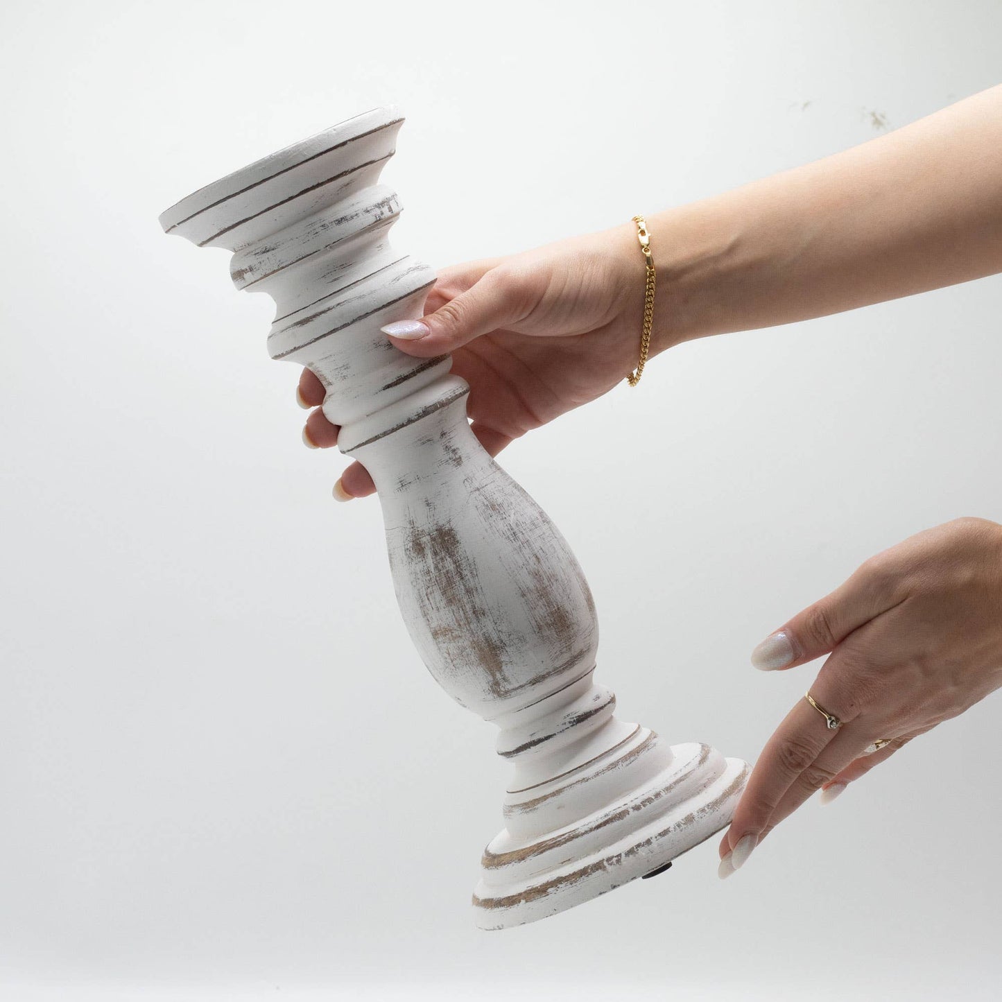 Person holding a white distressed candle holder against a light background
