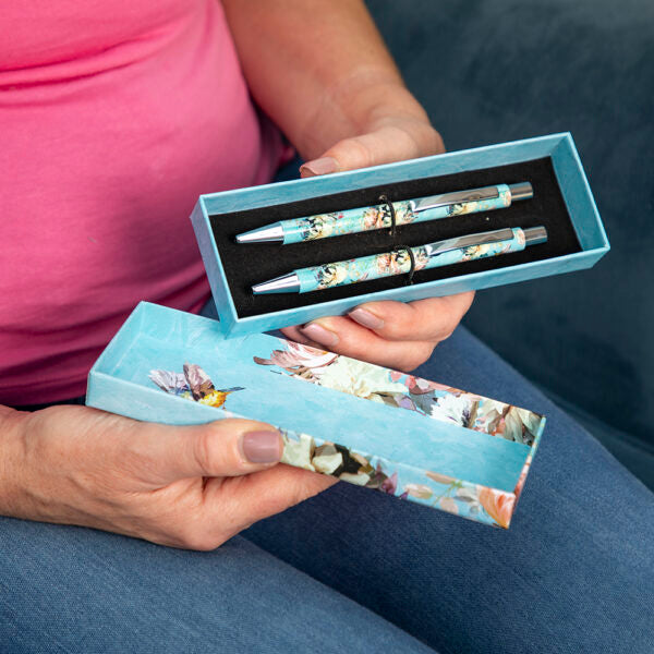 Person holding a set of floral-patterned pens in a matching box.