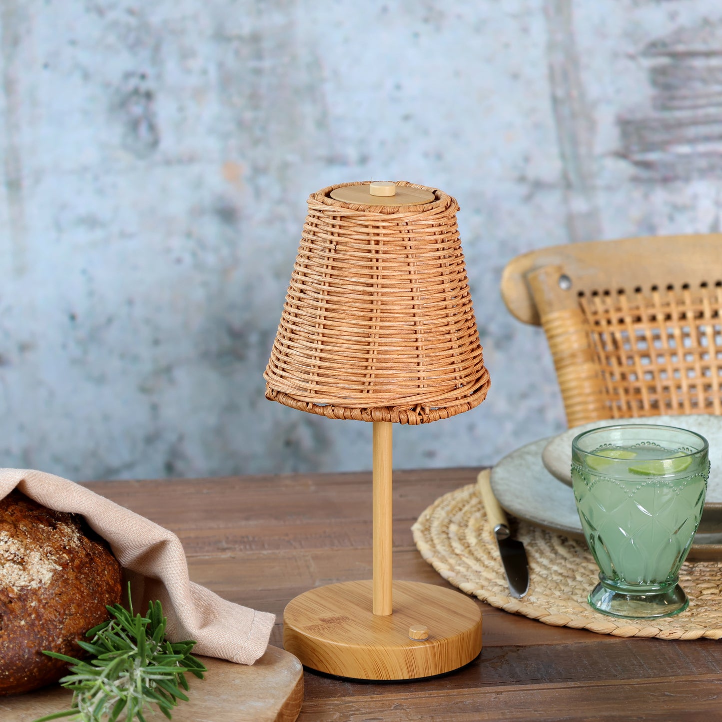 Wicker table lamp on a wooden table with bread and a glass of water.