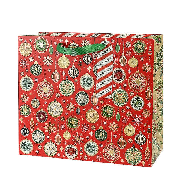 A red Christmas gift bag decorated with an all-over pattern of gold, green, and white ornaments, snowflakes, and stars, featuring green ribbon handles.