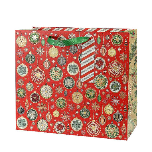 A red Christmas gift bag decorated with an all-over pattern of gold, green, and white ornaments, snowflakes, and stars, featuring green ribbon handles.