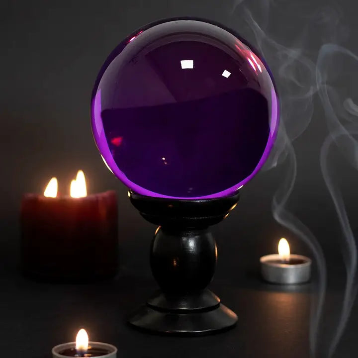 Purple crystal ball on a stand with candles in the background