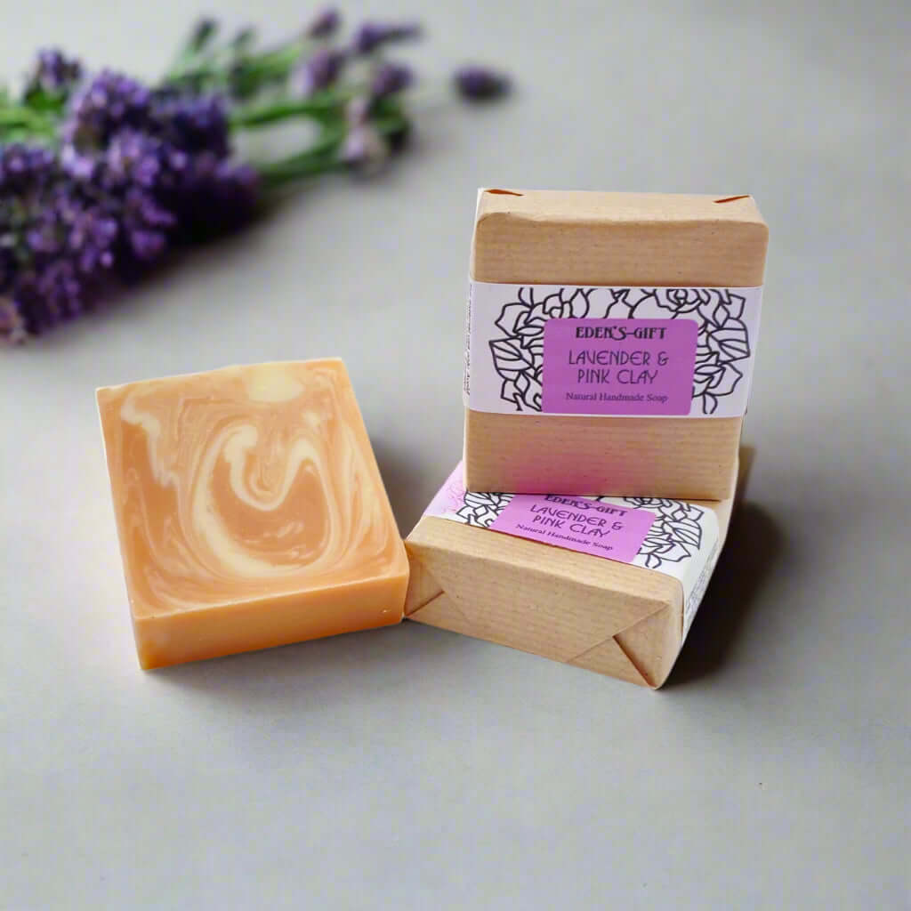A packaged handmade soap bar with a label indicating 'Lavender & Pink Clay'. The bar is beige in color with a purple and black floral pattern on the label.