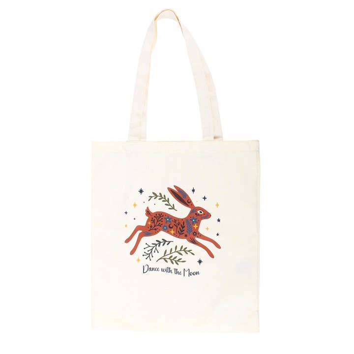 An off-white canvas tote bag featuring a whimsical illustration of a hopping rabbit in orange, blue, and purple, surrounded by small stars and leaves, with the text 'Dance with the Moon' printed below.